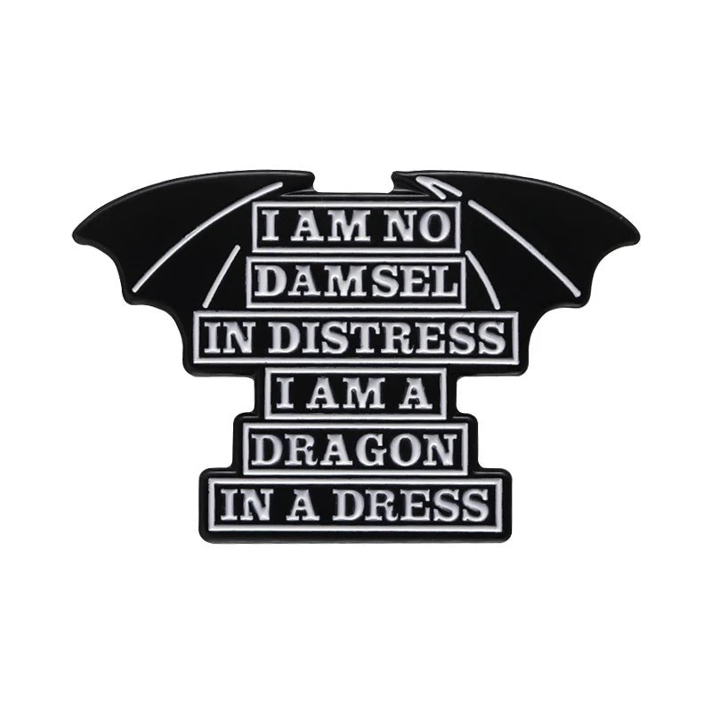 Black enamel pin features dragon wings and white text: “I am no damsel in distress, I am a dragon in a dress”—a bold addition to any feminist pin collection.