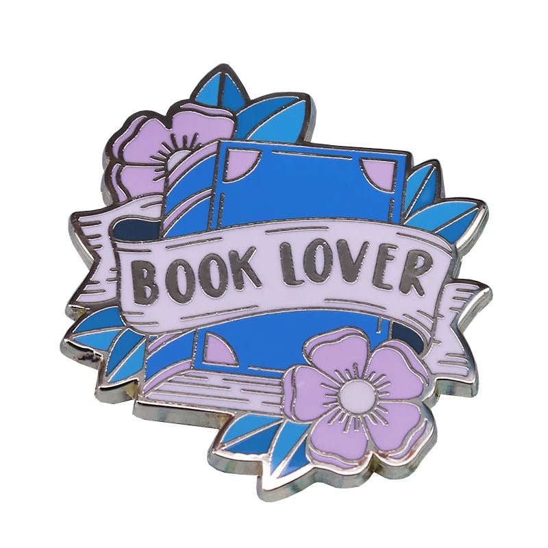 A blue enamel pin features a blue book with a BOOK LOVER banner, pink and purple flowers, green leaves—perfect for any proud Sword Lesbian’s collection.