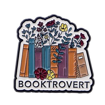 Enamel pin showcases colorful books and flowers above BOOKTROVERT in bold black letters, celebrating the magic of fictional characters and public libraries with a playful design on a white background.
