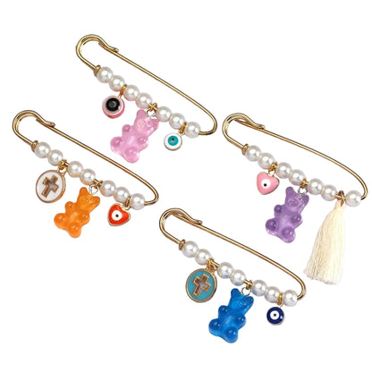 Kiss Me Laters baby brooch set features four gold safety pins adorned with faux pearls, gummy bear charms, beaded eye motifs, cross designs, and a white tassel—an eye-catching gift for baby showers.