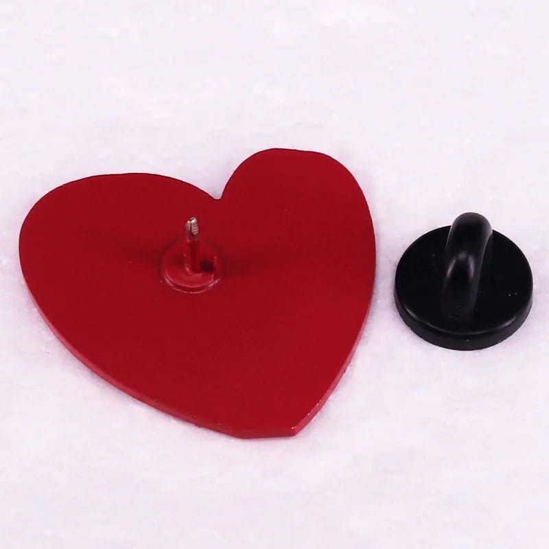 A red, heart-shaped pin with a metal post rests on a white surface beside a round black backing—ideal for pairing with your favorite neurodiversity or Too Cute To Be Neurotypical enamel pin.