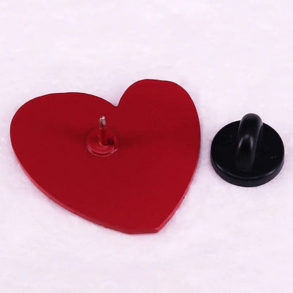 A red, heart-shaped pin with a metal post rests on a white surface beside a round black backing—ideal for pairing with your favorite neurodiversity or Too Cute To Be Neurotypical enamel pin.