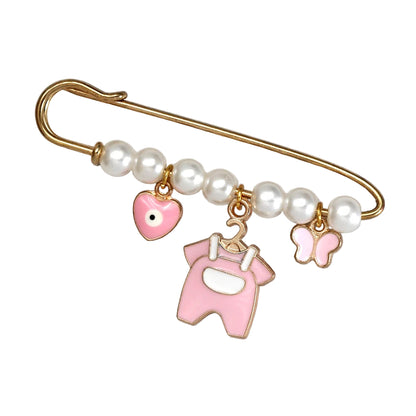 The Kiss Me Later gold safety pin brooch features white pearls and three pink charms—a heart, baby onesie, and butterfly—making it a charming beads and charms accessory, perfect as a unique baby shower gift. Displayed on a white surface.
