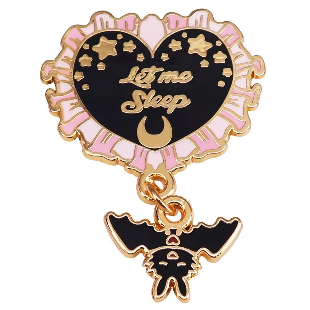 The My Cutesy Era Let Me Sleep enamel pin features a pink and black heart with gold and black enamel, pink frills, stars, a gold crescent moon, and a dangling black bat charm—perfect for night owls!.