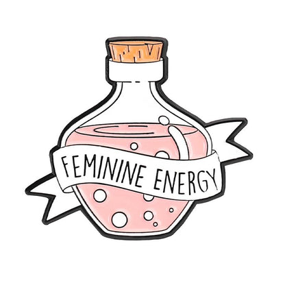 A glass potion bottle with a cork stopper holds pink liquid and bubbles. A white ribbon wraps the bottle, boldly reading Feminine Energy. This empowering enamel pin  stands out against a crisp white background.