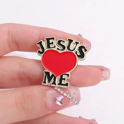 A hand with decorated nails holds a cute pink enamel pin from Kiss Me Later that says JESUS ❤️ ME, with a red heart symbol for loves.