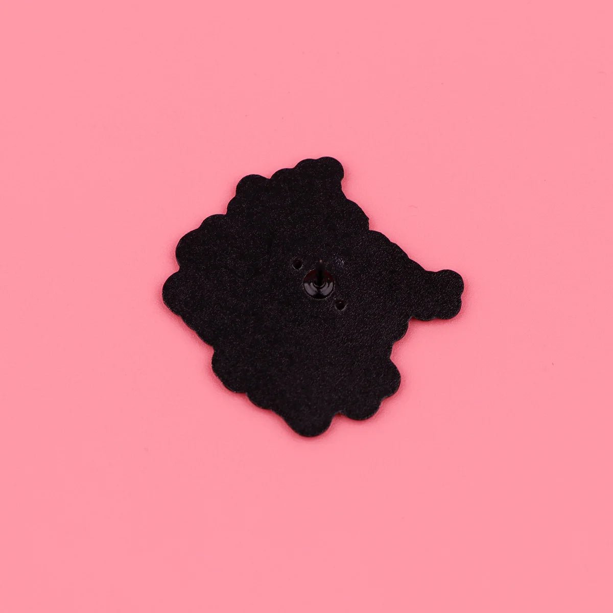 Black, irregularly-shaped motivational enamel pin with scalloped edges and a shiny bump sits on a pink background—an uplifting gift idea for coworkers.