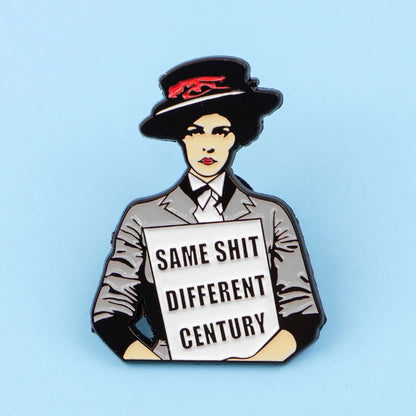 The Kiss Me Later enamel pin features a woman in vintage attire and hat, holding a SAME SHIT DIFFERENT CENTURY sign on a light blue background—a modern twist on the classic suffragette pin.