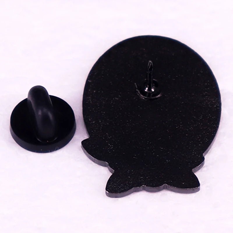 Black floral enamel pin with butterfly clutch backing is shown from the back on a light surface. This white oval pin has small protrusions at the bottom for added detail.