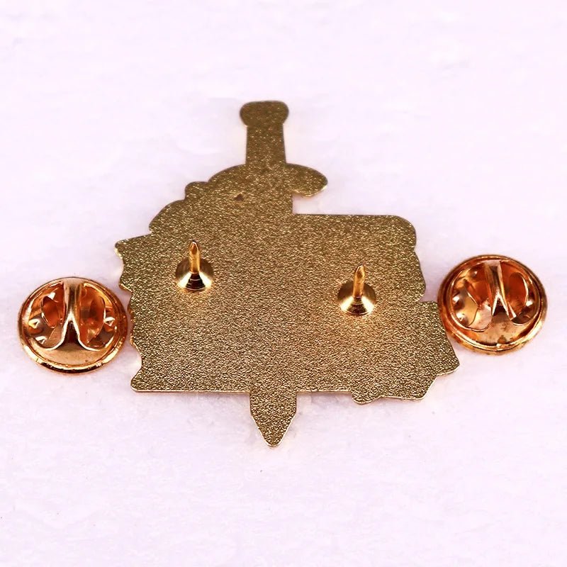 A gold metal enamel pin seen from the back with two butterfly clutch fasteners and three pointed pin posts on a textured surface—a subtle nod to Enemies To Lovers stories for romance fans.