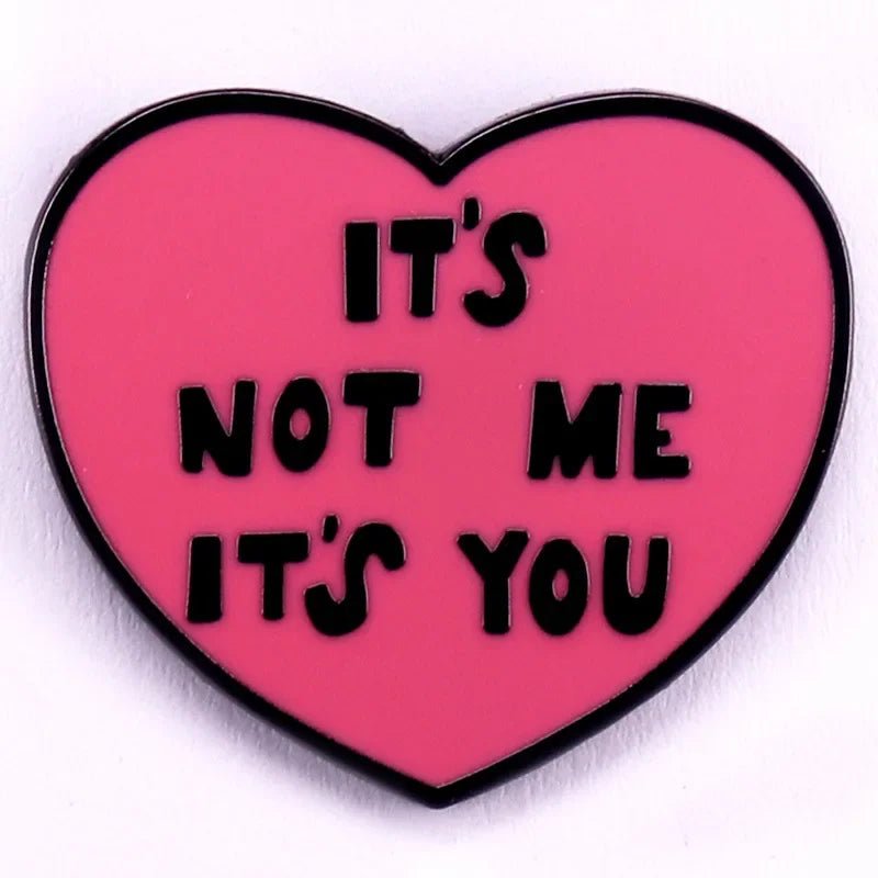 Red pink love heart enamel pin with the bold phrase “ITS NOT ME ITS YOU” in striking black letters.