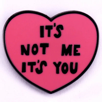 Red pink love heart enamel pin with the bold phrase “ITS NOT ME ITS YOU” in striking black letters.
