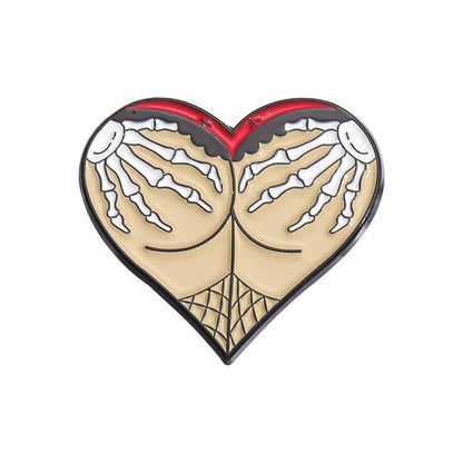 Gothic heart-shaped pin features two skeleton hands grabbing rounded shapes resembling buttocks, accented with a fishnet pattern at the bottom. Its bold, edgy design stands out against the plain white background.