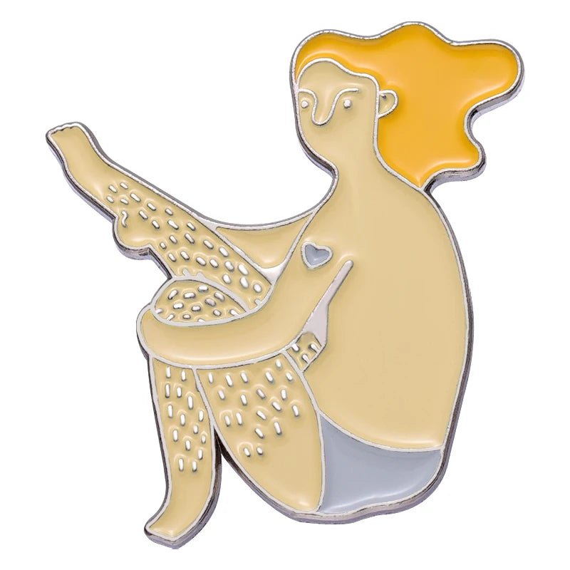 enamel pin features a person with long orange hair, visible body hair, a love heart on their arm, and gray shorts. Designed in pale yellow and gray tones, it celebrates self love with unique charm.