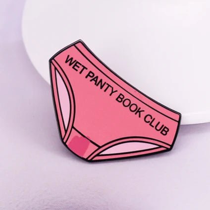 pink enamel pin shaped like womens underwear with Wet Panty Book Club across the front, ideal for book club lovers, shown on a light purple surface.