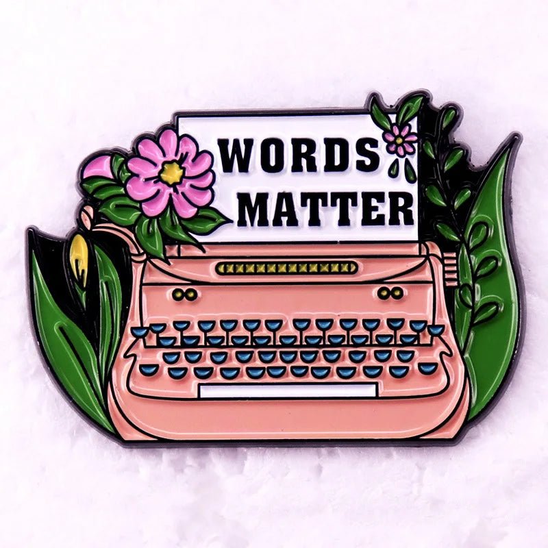 A charming enamel pin — a pink typewriter with floral accents and a paper reading WORDS MATTER in bold, perfect for Romance Readers or book lover badge collectors.