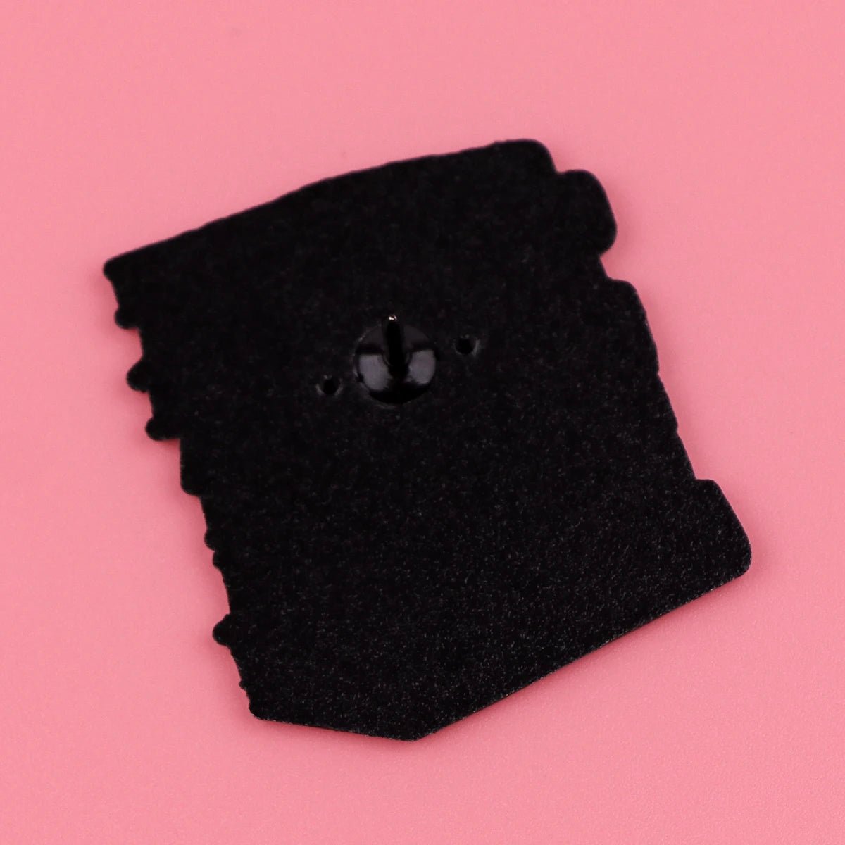 A unique, irregular black felt piece with a central black button displayed on pink—an ideal quirky treasure for booktroverts and fans of fictional characters.