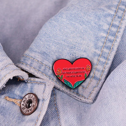 An enamel pin with a red heart, yellow flowers, and green leaves says shes gonna listen to her heart; its gonna tell her what to do—a perfect accessory for any denim jacket.n