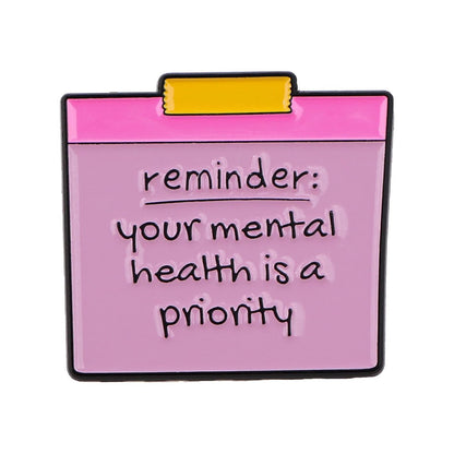 Pink clipboard-shaped pin features “reminder: your mental health is a priority” in black on a lavender background—an uplifting accessory for sharing positive affirmations and self-empowerment.