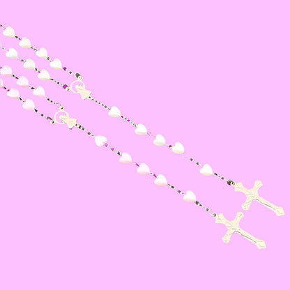 Two My Cutesy Era rosary necklaces with white heart-shaped beads and gold crucifixes, inspired by the Virgin Mary, are arranged diagonally on a pastel pink background.