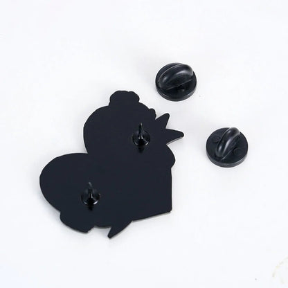 The Kiss Me Later black enamel pin features two heart-like shapes, two pointed pins on the back, and two detachable round black rubber pin backs, all displayed on a white surface—perfect as a heart or love pin.