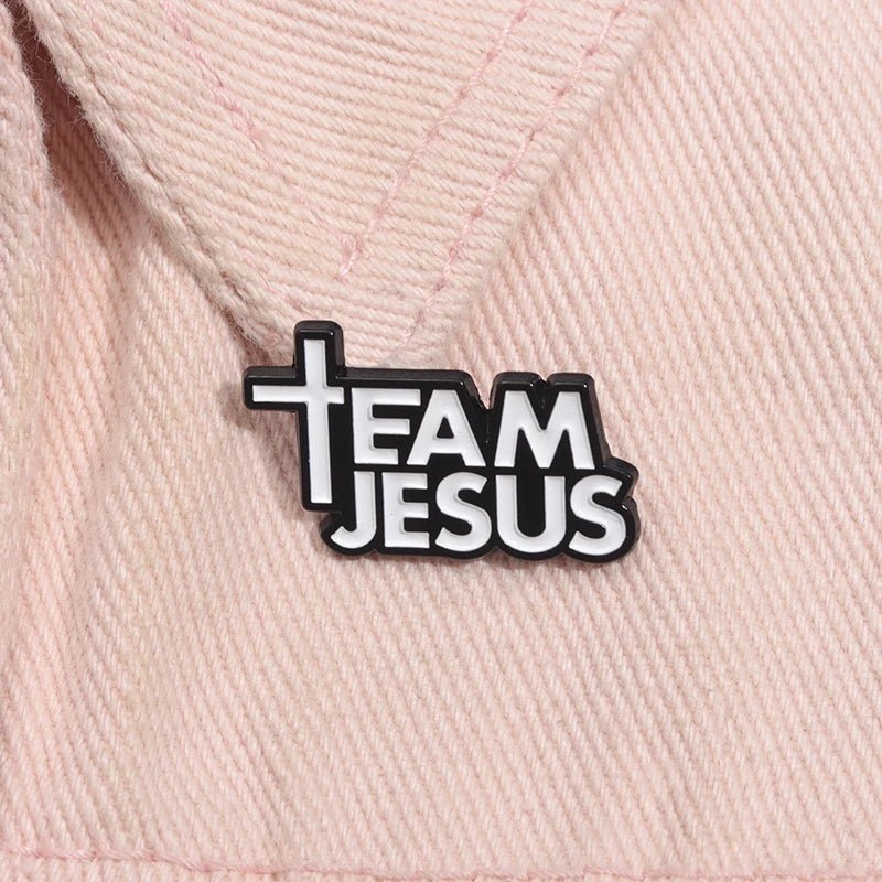 A black and white pin on light pink fabric reads TEAM JESUS, with the T shaped like a cross—a subtle nod to faith and Bible inspiration.
