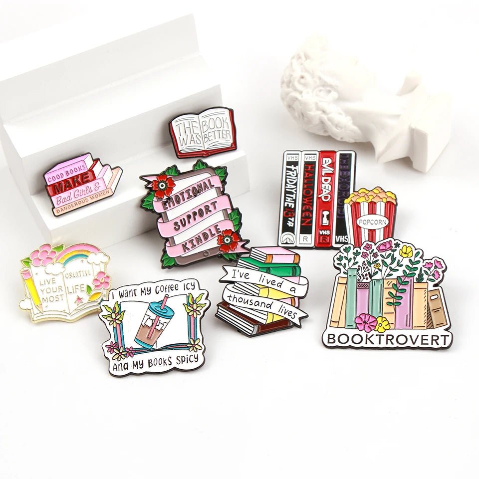 Enamel pins feature colorful book-themed designs perfect for romance readers—stacks of books, bookshelves, coffee, popcorn, flowers, and phrases like “Booktrovert” and “I want my coffee icy and my books spicy.”.