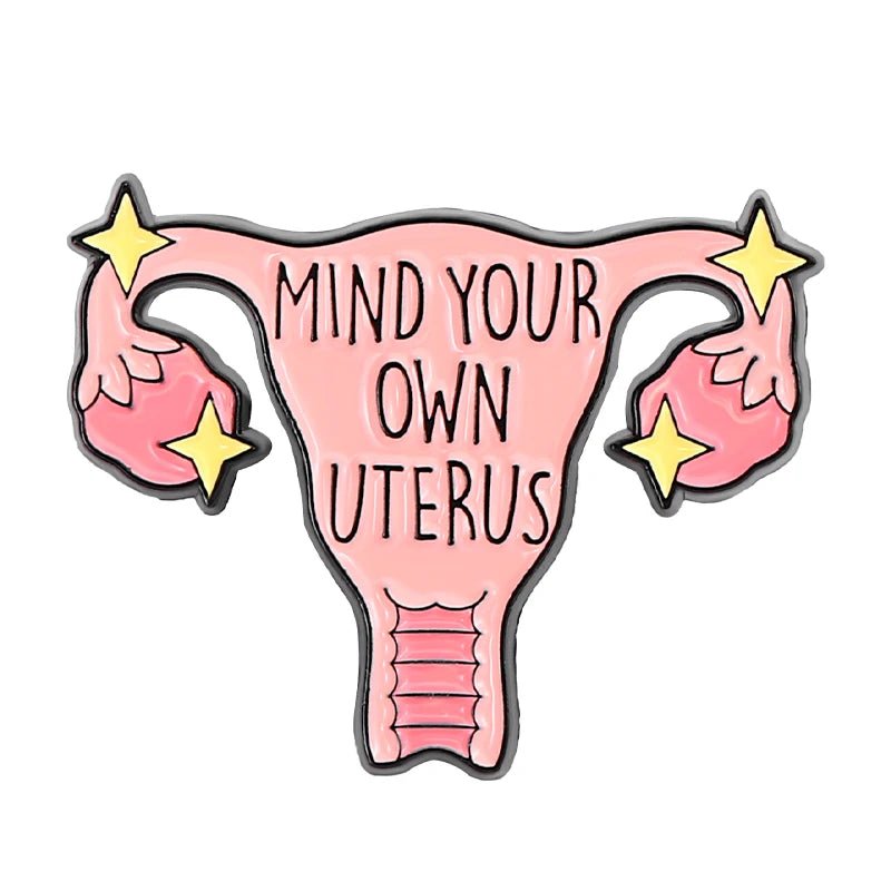 An illustration of a uterus with MIND YOUR OWN UTERUS inside, accented by yellow stars near the ovaries. This bold feminist pin features a white background.
