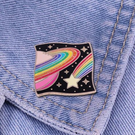 The Kiss Me Later enamel pin is a must-have trendy accessory, featuring a rainbow-striped planet with rings and a shooting star, perfect for adding flair to the collar of your light blue denim jacket.