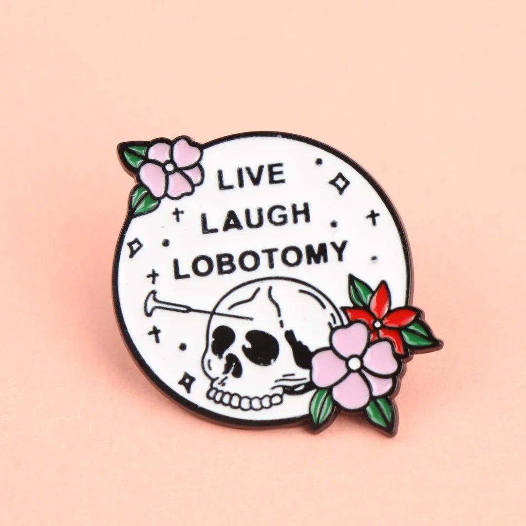 The Gay Skate round enamel pin features a skull with a nail in its head, surrounded by pink and red flowers. LIVE LAUGH LOBOTOMY stands out in bold on a white background—quirky flair for your collection!.