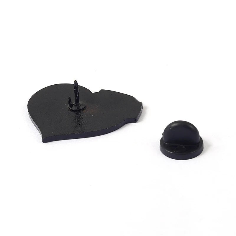 A black heart-shaped enamel pin with two pointed posts is displayed beside a black rubber pin backing on a white surface, ideal for pairing with your favorite Skeleton holding pink rose or pink milk carton enamel pin.