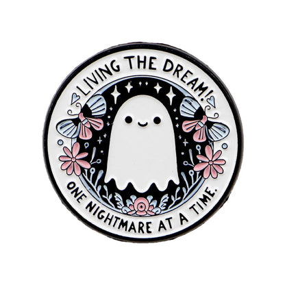 A pin that shows a cute ghost with flowers, stars, and two moths, surrounded by the phrase: LIVING THE DREAM! ONE NIGHTMARE AT A TIME.