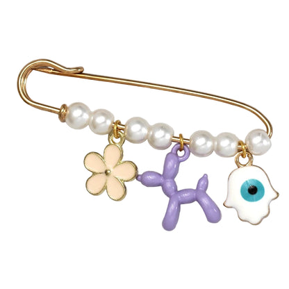 The Kiss Me Later gold safety pin brooch features white pearls and three charms—a cream flower, purple balloon dog, and white evil eye—making it a charming beads and charms accessory, ideal as a baby shower gift.