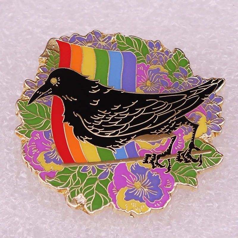 Enamel pin stands in front of a rainbow with green leaves and purple flowers behind it, all outlined in gold.