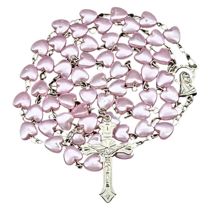 The My Cutesy Era rosary necklace features pink heart-shaped beads, a silver crucifix, and a Virgin Mary medallion, all elegantly arranged in a circular pattern.