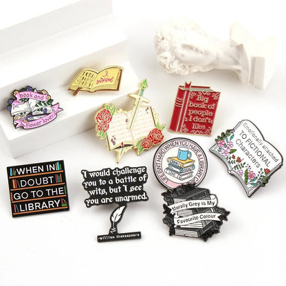 A collection of colorful enamel pins and book lover badges with book and literature themes is arranged on a white surface next to a small bust statue—perfect literary designs for any Romance Reader.