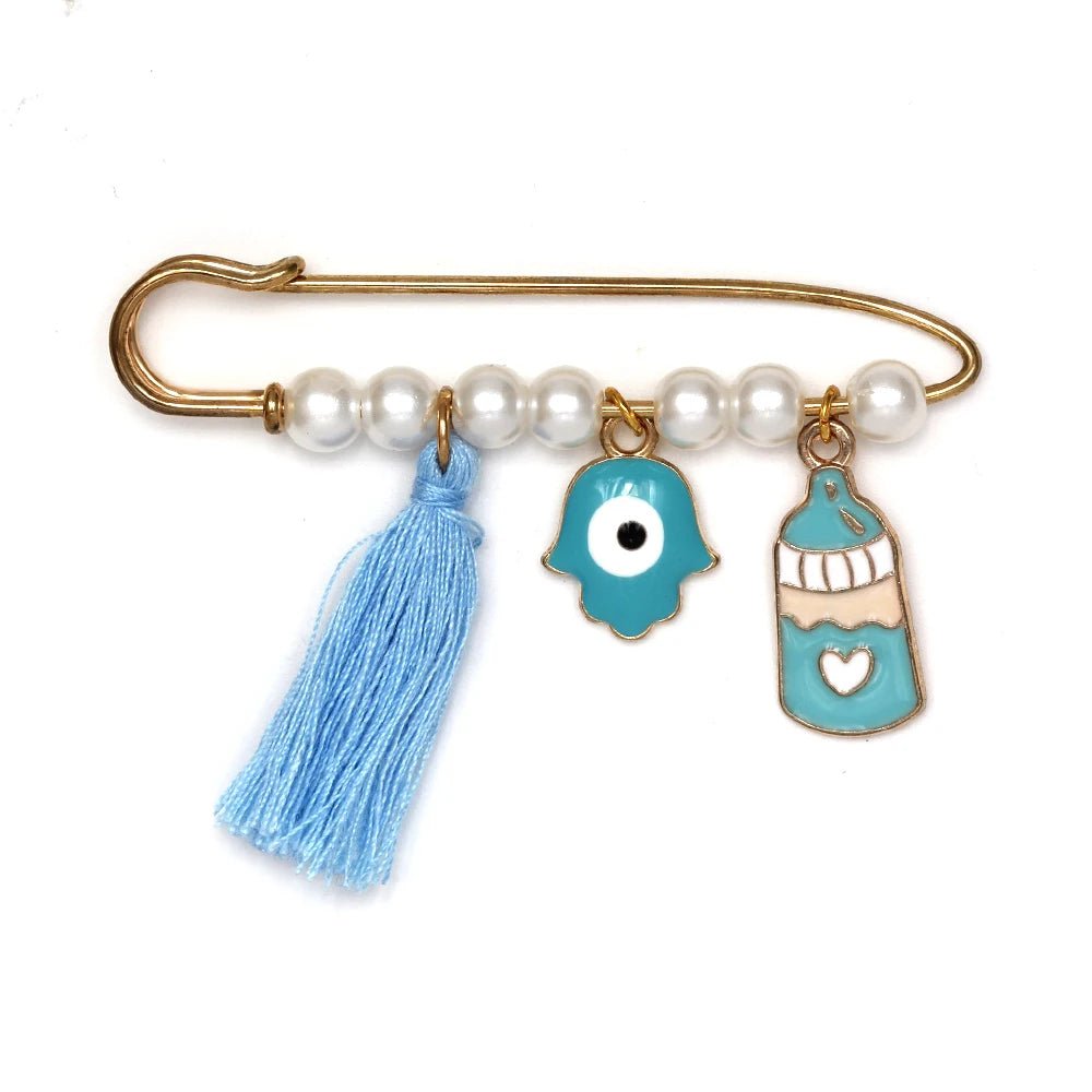 The Kiss Me Later decorative gold safety pin features white pearls, a light blue tassel, a blue hamsa evil eye charm, and a blue and white baby bottle—ideal as a baby shower gift or unique brooch.