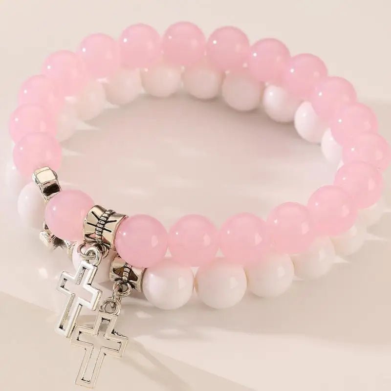 Two crystal bead bracelets—one pink, one white—from Kiss Me Later are stacked together, each with a silver Cross charm. The light background highlights these stylish Christian stone bracelets.
