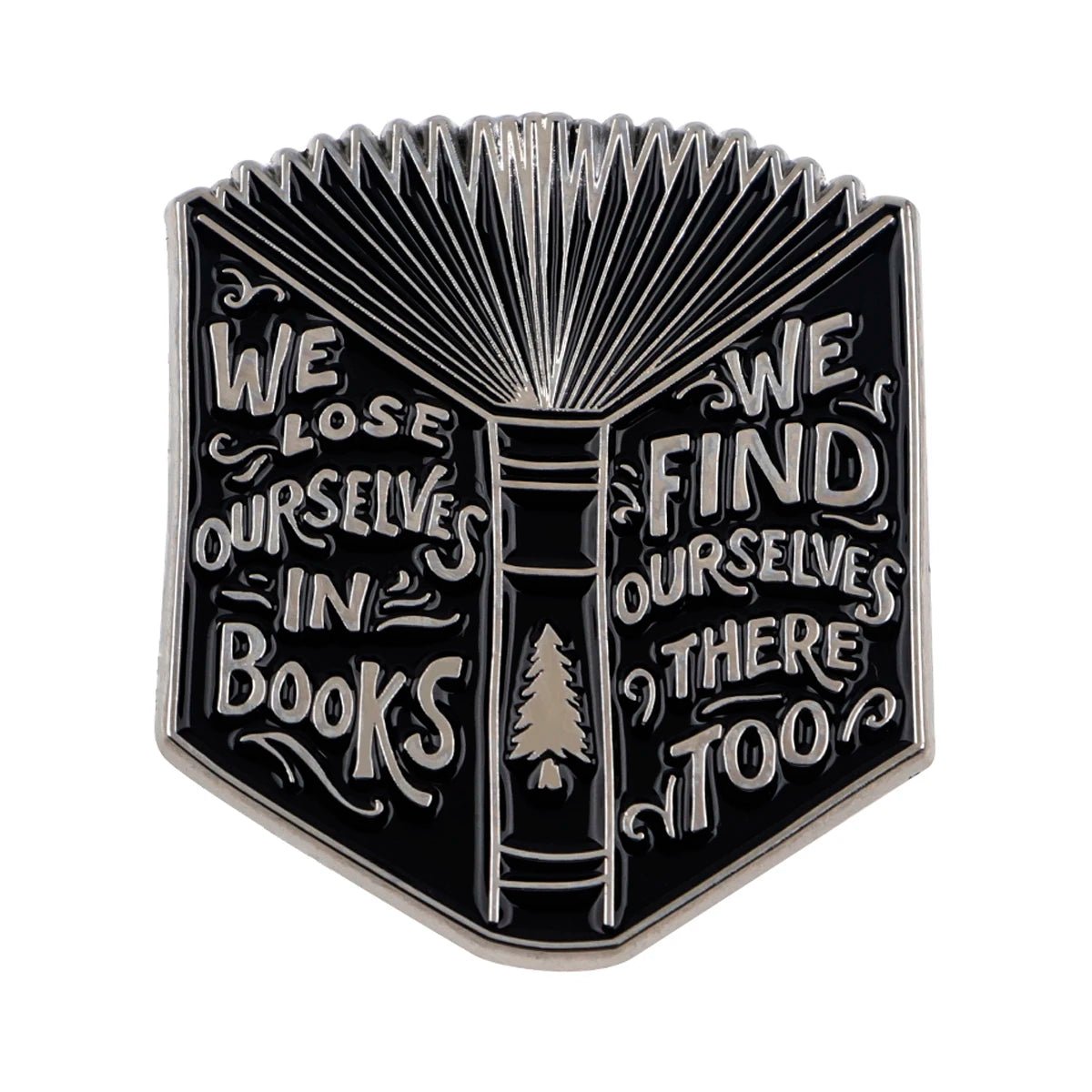 A black and silver metal pin shaped like an open book with We lose ourselves in books, we find ourselves there too engraved and a small tree on the spine—perfect for booktroverts.
