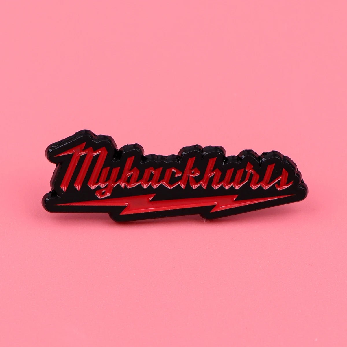 A My Back Hurts enamel pin features Mybackhurts in red script with a black outline, a red lightning bolt below, and a pink background—a bold accessory for statement style.