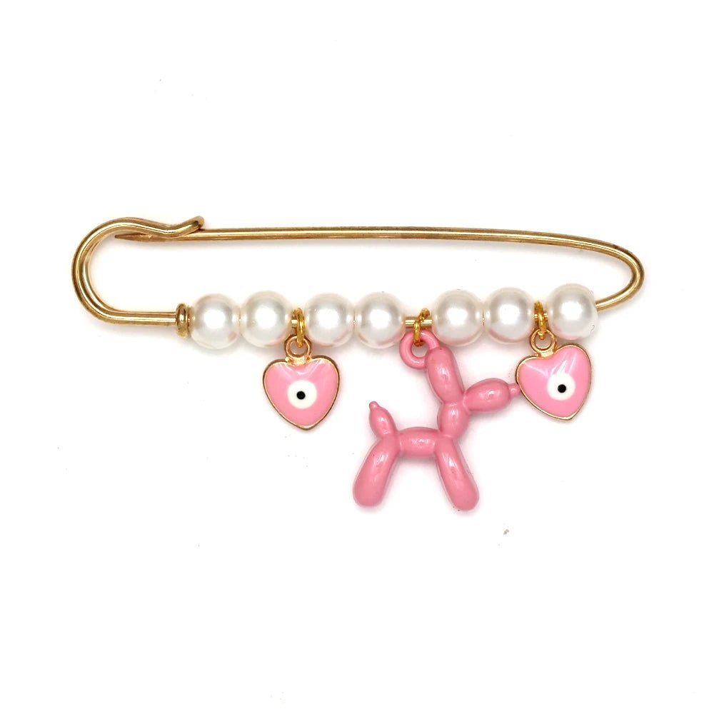 The Kiss Me Later gold safety pin brooch features white pearls and three dangling charms—two pink heart-shaped charms with eyes and a central pink balloon dog—making it a whimsical, charming gift for baby showers.