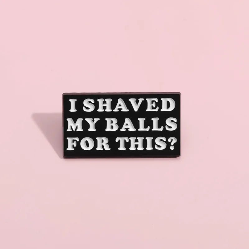 A rectangular black and white enamel pin featuring bold white text I SHAVED MY BALLS FOR THIS?, is shown on a plain light pink background.