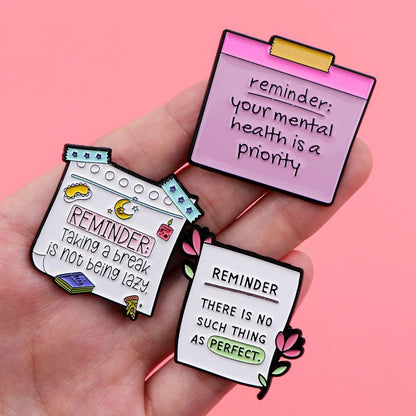 A hand holds three colorful note-shaped pins by with mental health affirmations—your well-being is a priority, taking breaks isnt lazy, and theres no such thing as perfect—set against a pink background.