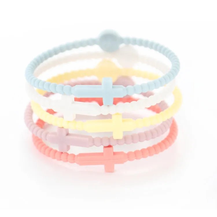 Kiss Me Later’s set of four silicone beaded bracelets in pastel blue, white, yellow, and pink—each with a matching cross charm—are stacked together on a white background. A charming Cutie Bracelet to celebrate Jesus.
