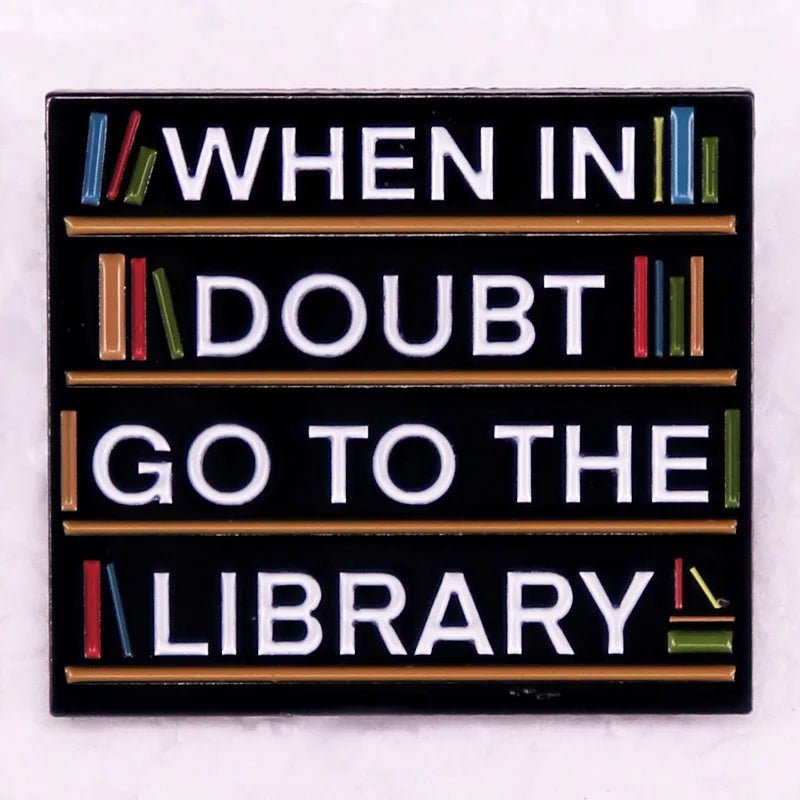 Enamel pin shows white text on black—WHEN IN DOUBT GO TO THE LIBRARY—with colorful books along the edges, ideal for book lovers and pin collectors.