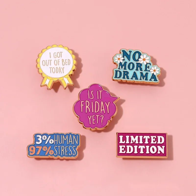 Five colorful enamel pins, including a red love heart, on a pink background. Fun phrases: I got out of bed today, No more drama, Is it Friday yet?, 3% human 97% stress, and Limited edition. Cute but psycho vibes!.