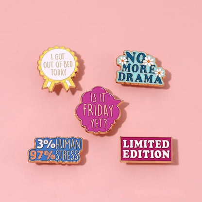 Five colorful enamel pins, including a red love heart, on a pink background. Fun phrases: I got out of bed today, No more drama, Is it Friday yet?, 3% human 97% stress, and Limited edition. Cute but psycho vibes!.