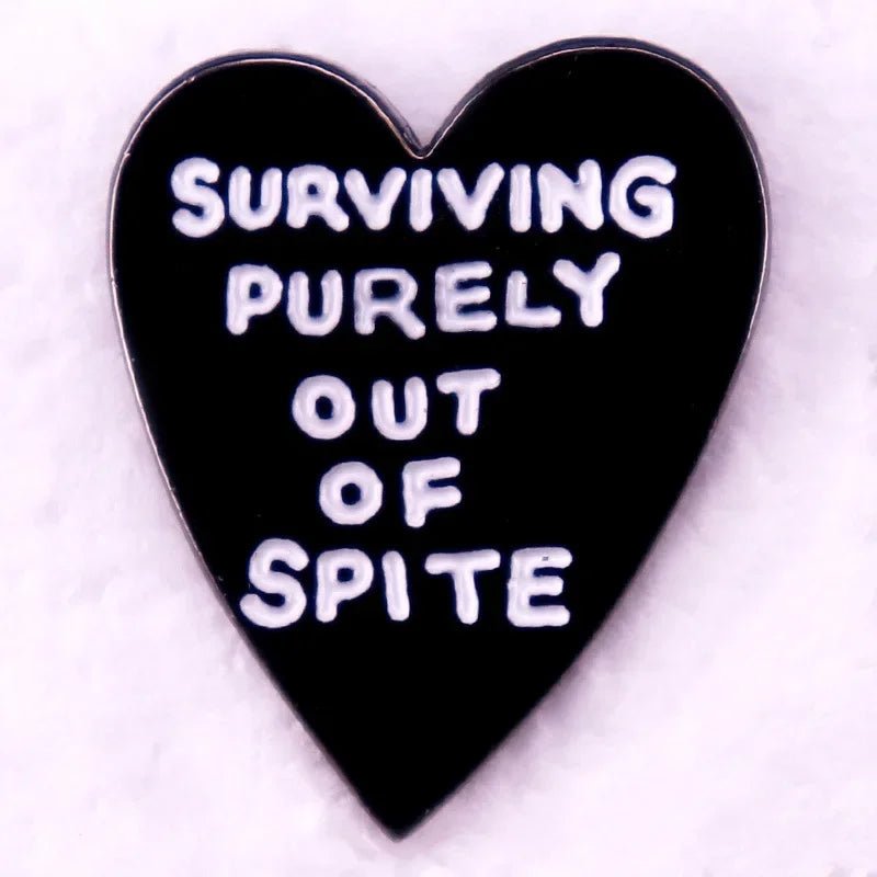 A pink enamel pin featuring a love heart and white text that says Surviving purely out of spite, displayed on a soft, pale background.