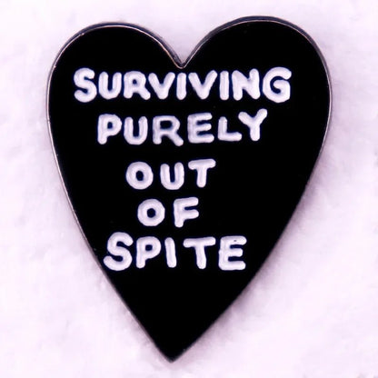 A pink enamel pin featuring a love heart and white text that says Surviving purely out of spite, displayed on a soft, pale background.