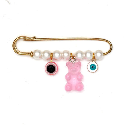 The Kiss Me Later gold safety pin brooch features five white pearls and three dangling charms—a pink gummy bear, a pink circle, and a blue evil eye—making it a unique beads and charms accessory, perfect for baby shower gifting.